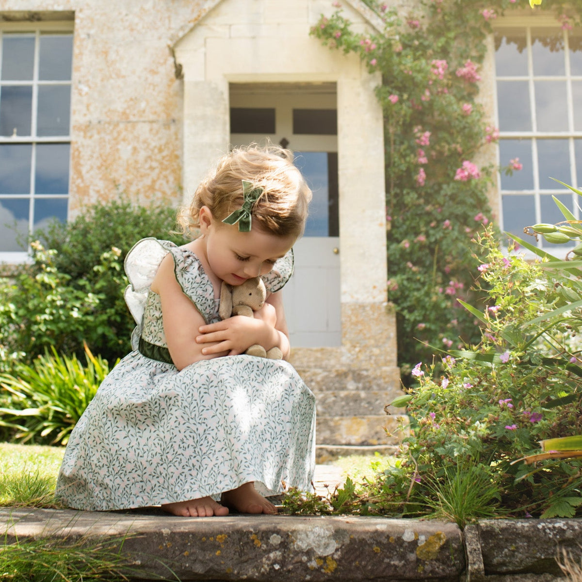 Young girl in a floral dress holding a rabbit in a garden setting.