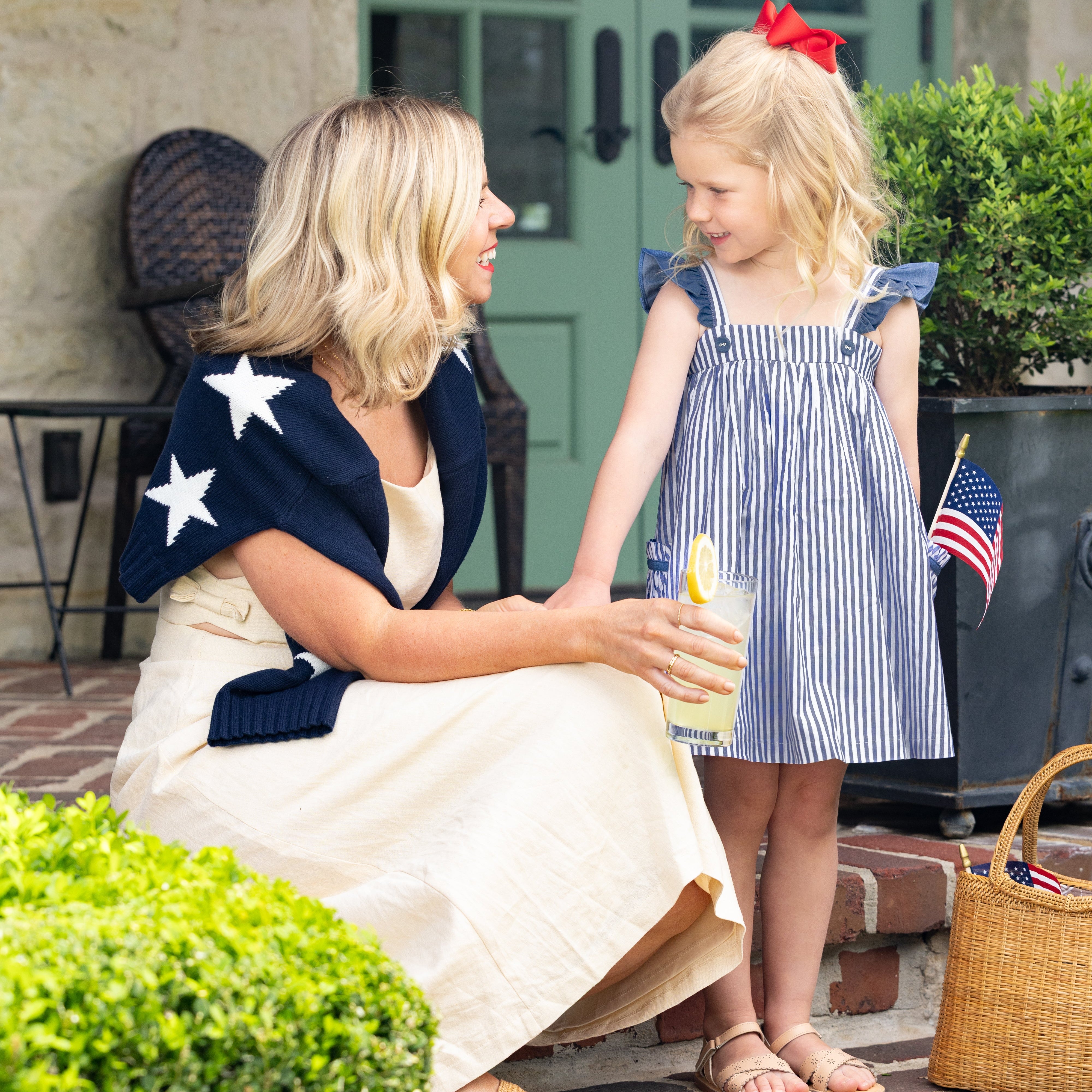 Woman and young girl sitting on a step outdoors, both wearing patriotic outfits.