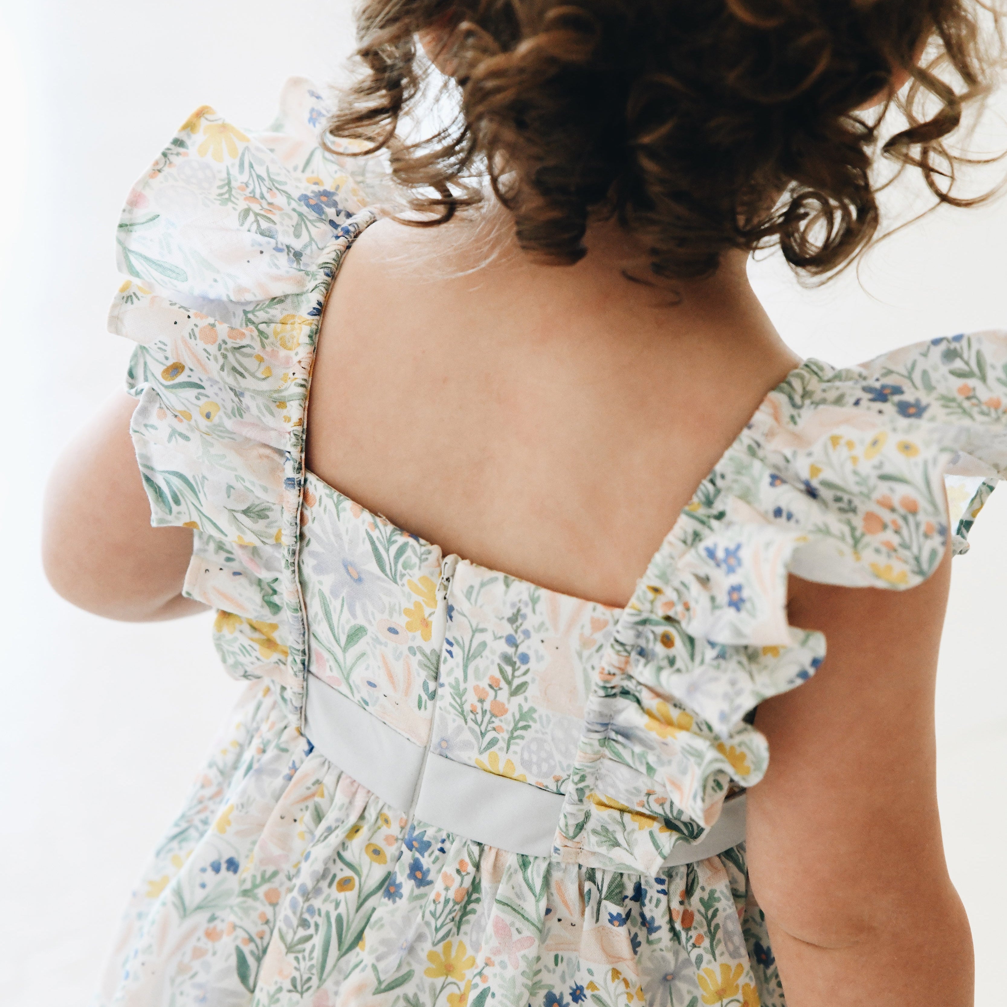 Child wearing a floral dress with ruffled sleeves on a neutral background