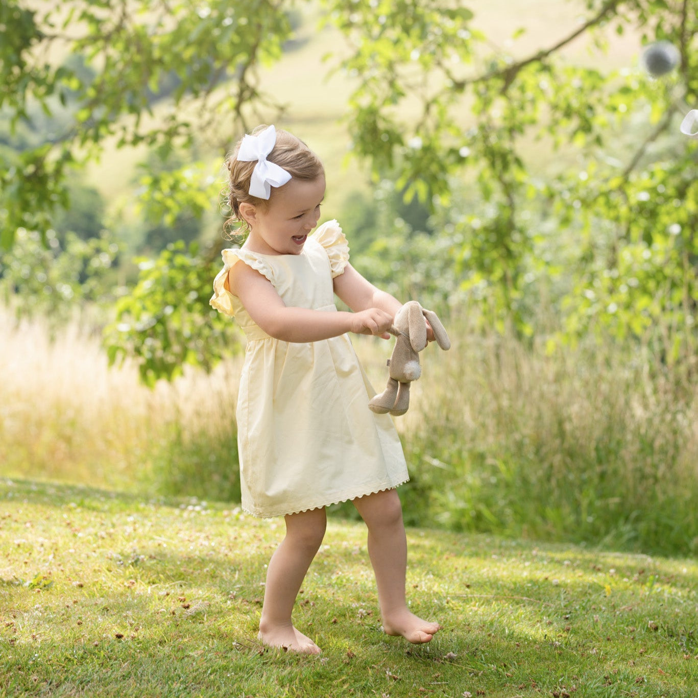 Young girl in a yellow dress standing in a grassy field with trees in the background